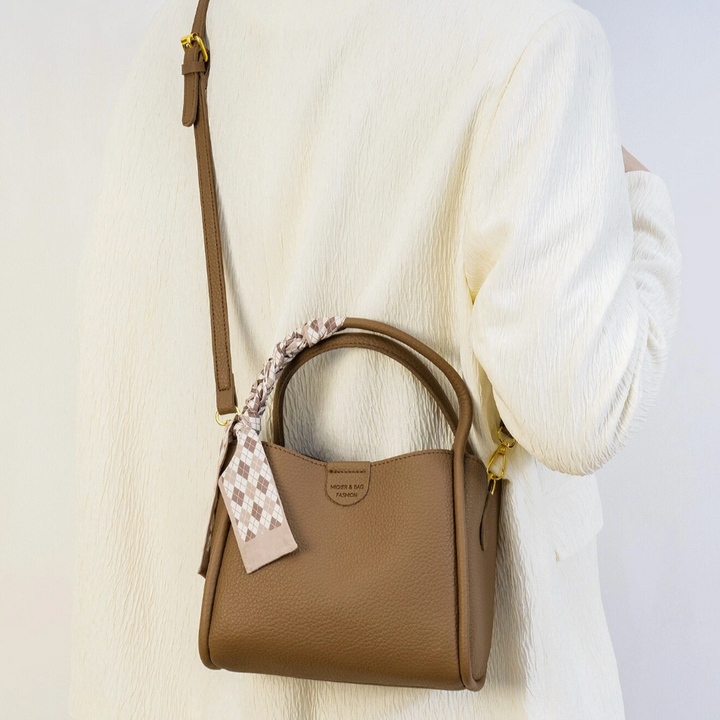 Borsa a tracolla marrone in pelle, indossata su spalla, con foulard decorativo. Elegante accessorio moda donna, perfetto per ogni occasione.