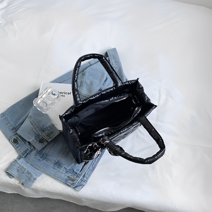 Borsa nera in pelle su letto bianco con giacca di jeans e libro. Accessori moda donna, stile casual chic.