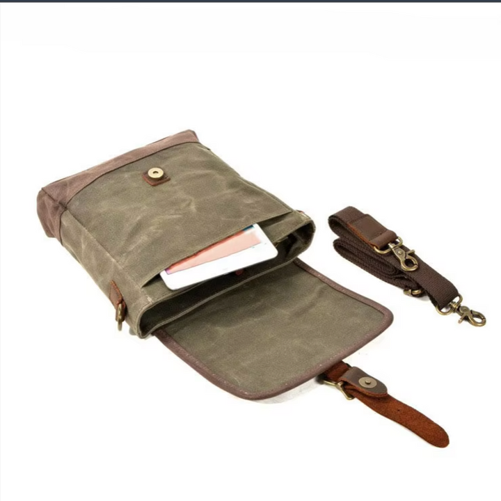 Borsa a tracolla in tela cerata verde con chiusura a bottone, tasca interna per smartphone e tracolla regolabile marrone. Accessorio moda unisex.