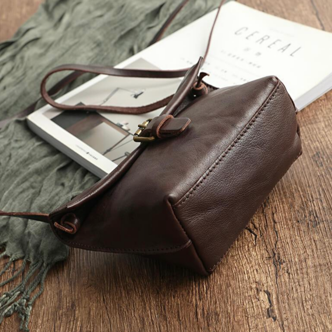 Borsa a tracolla in pelle marrone su tavolo di legno, con rivista e sciarpa verde. Elegante accessorio moda donna, stile vintage.