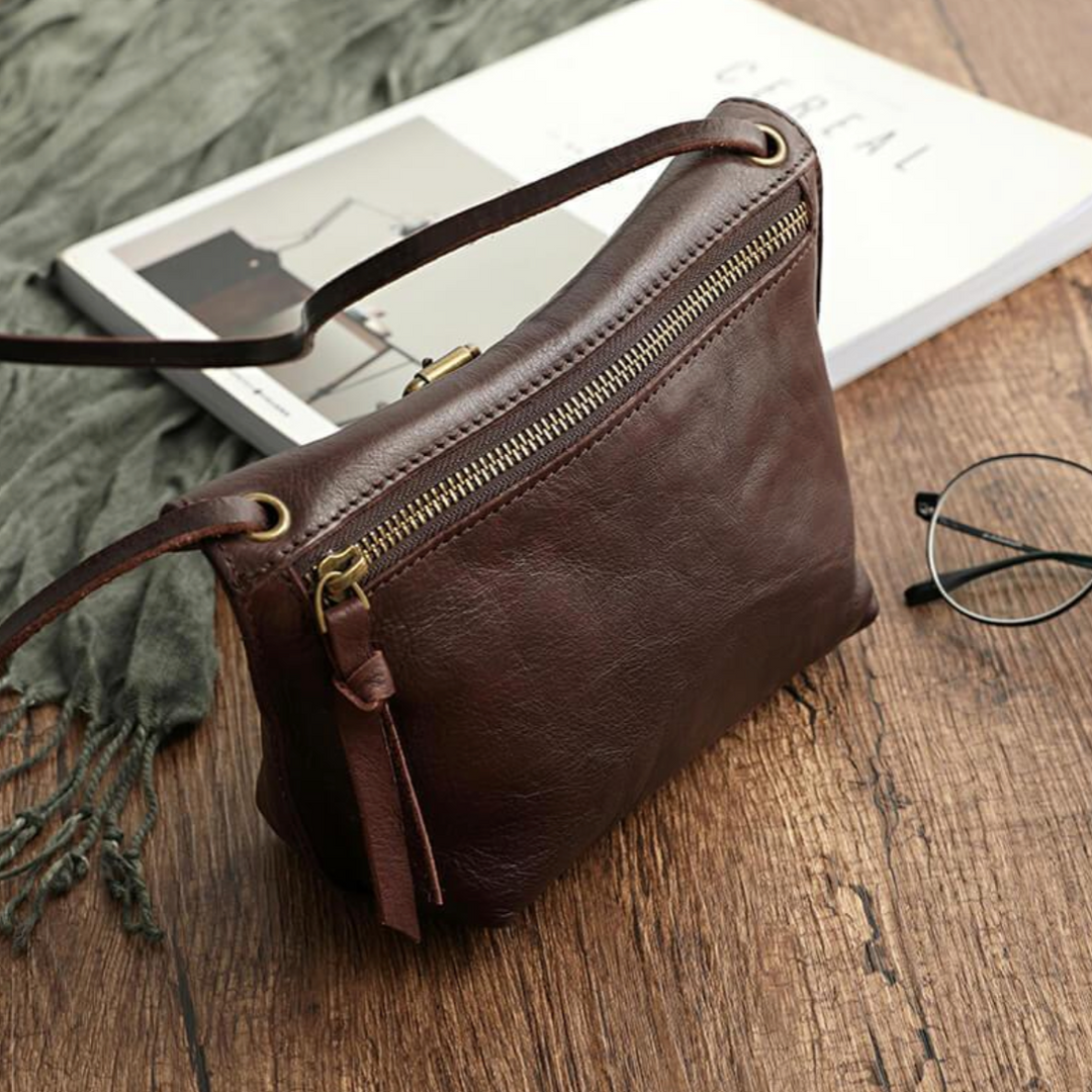 Borsa a tracolla in pelle marrone su tavolo di legno, accanto a occhiali e rivista. Elegante accessorio moda donna, stile vintage.