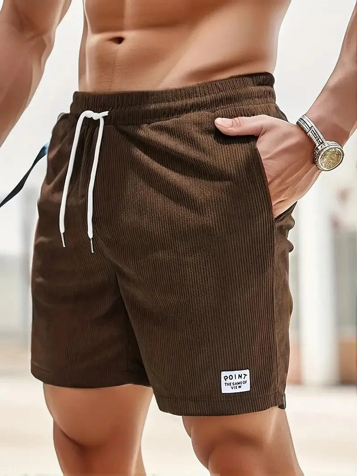 Shorts da uomo marroni in tessuto a coste, con laccio bianco in vita e tasche laterali. Ideali per moda estiva e casual.