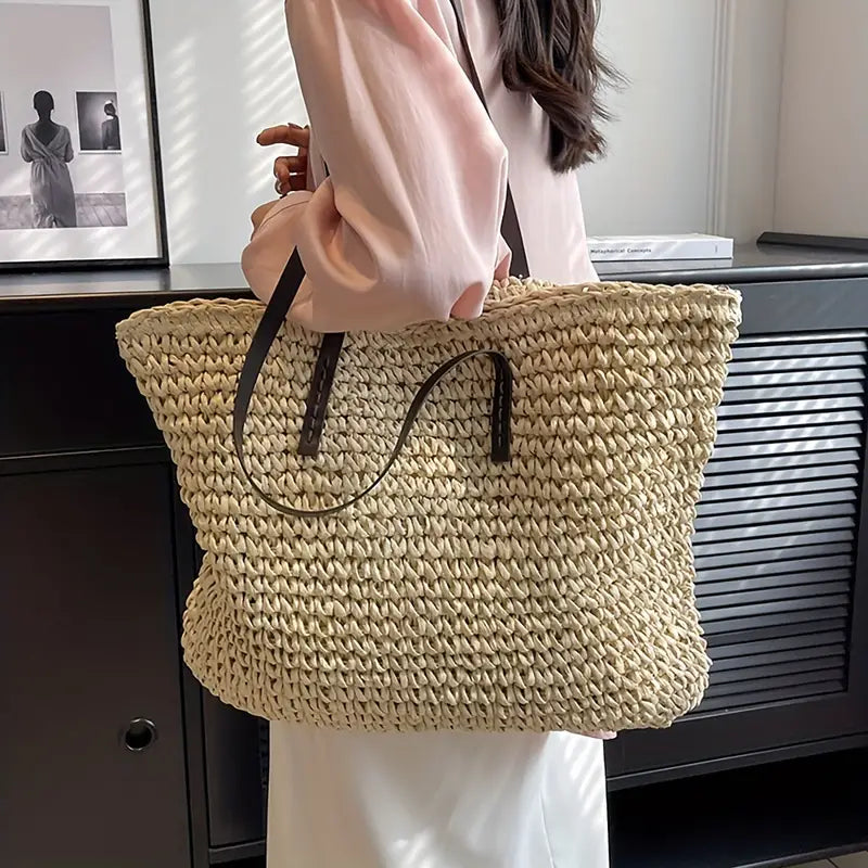 Donna con borsa di paglia intrecciata grande, manici in pelle marrone, indossa camicia rosa e gonna bianca. Accessorio moda estivo elegante.