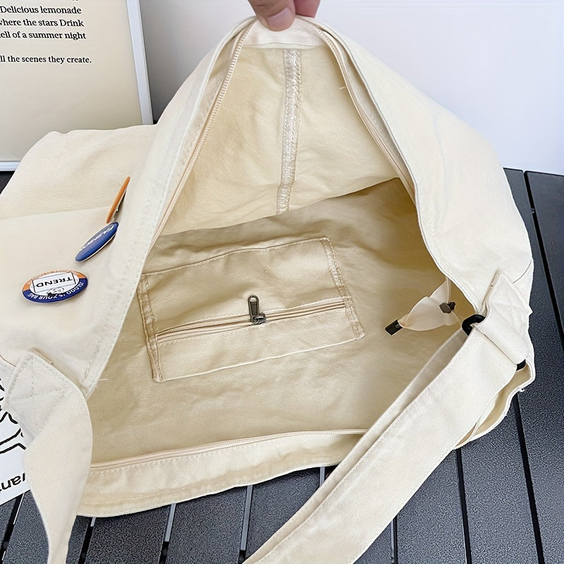 Borsa a tracolla in tela beige aperta, con tasca interna con zip, su tavolo grigio. Accessorio moda casual, spazioso e versatile.