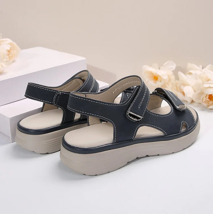 Sandali da donna in pelle nera con suola spessa beige, chiusura a strappo, design casual estivo, sfondo con fiori bianchi.
