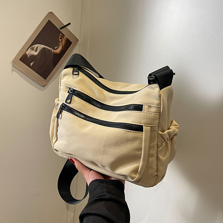 Borsa a tracolla beige con doppie cerniere nere, design moderno e funzionale. Accessorio moda unisex, ideale per viaggi e uso quotidiano.