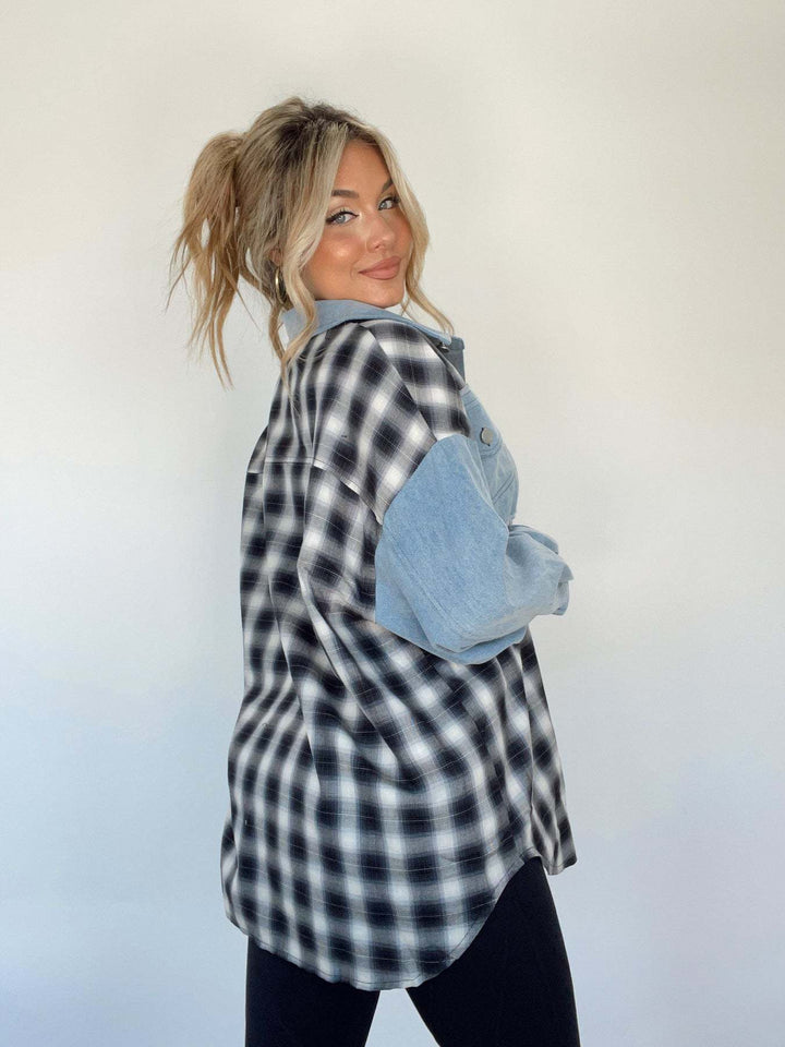 Donna con camicia a quadri bianca e nera e maniche in denim, capelli biondi raccolti, posa di profilo su sfondo bianco. Moda casual femminile.