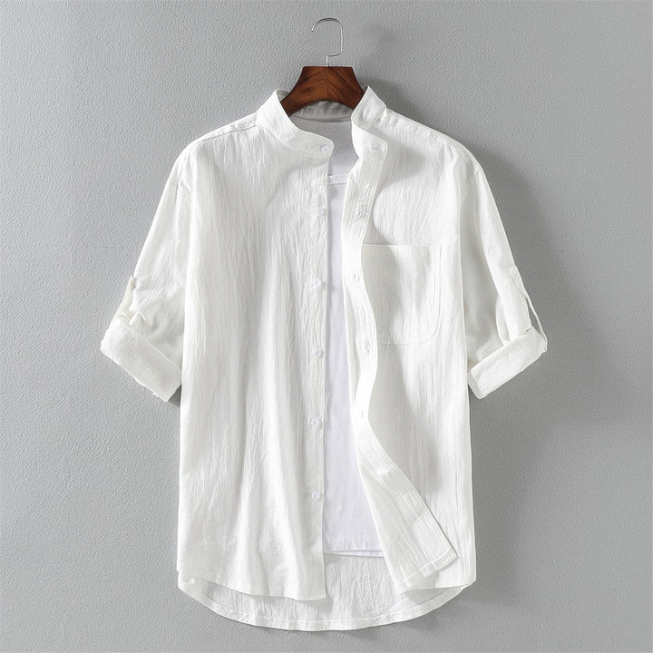 Camicia bianca da uomo in cotone, maniche lunghe arrotolate, colletto alla coreana, design casual elegante, appesa su gruccia.