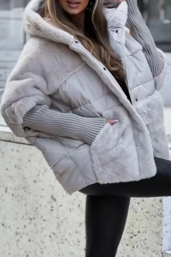 Cape d'hiver noire matelassée avec capuche, col en fausse fourrure et poches latérales.