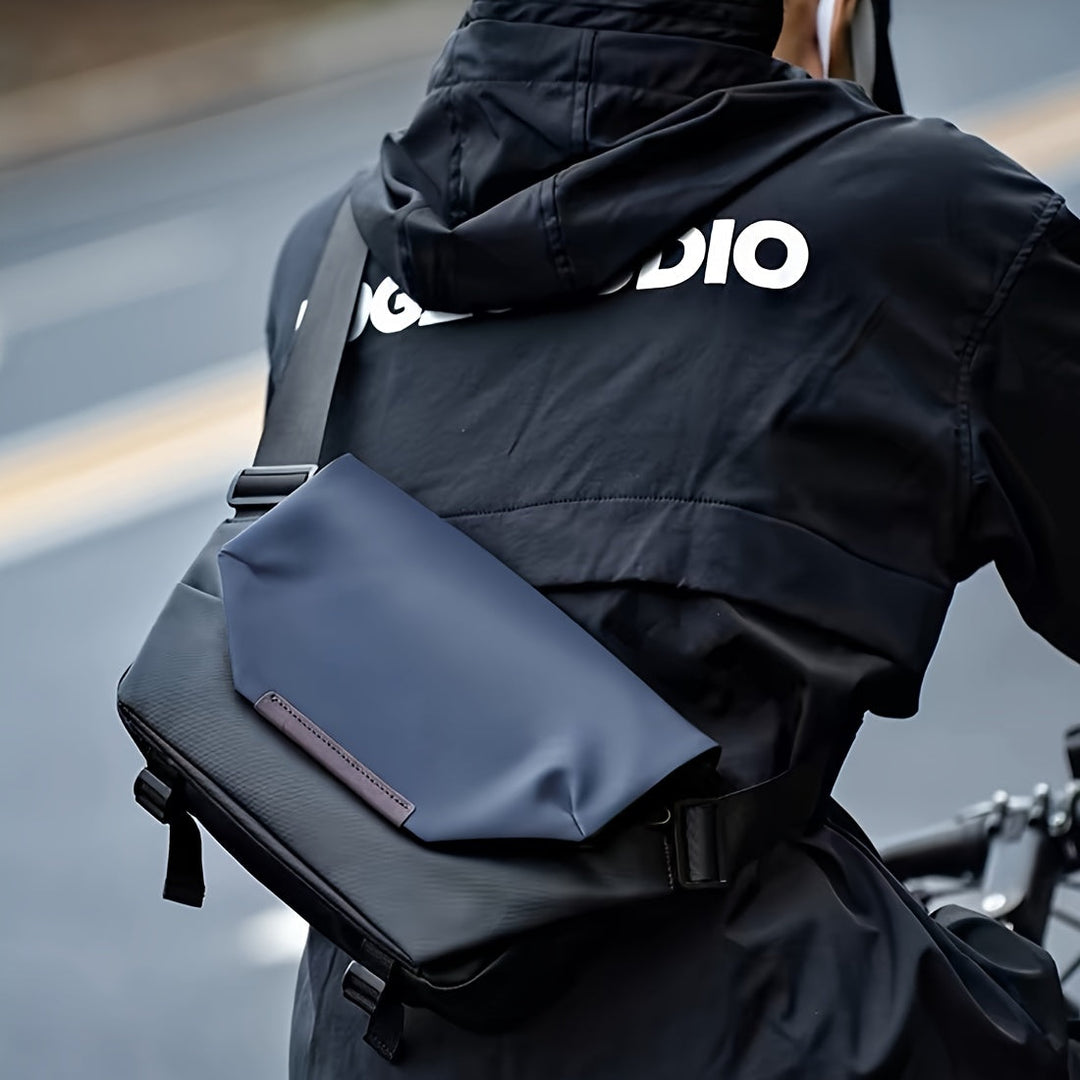 Giacca nera impermeabile con logo bianco, indossata da ciclista. Borsa a tracolla blu scuro, design moderno, ideale per ciclismo urbano.