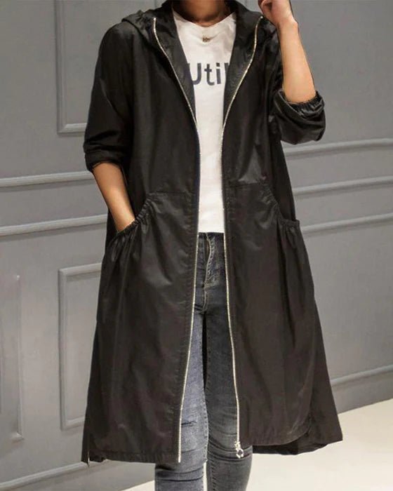 Giacca a vento nera da donna con cappuccio, zip frontale, tasche laterali, indossata su t-shirt bianca e jeans. Moda casual autunnale.