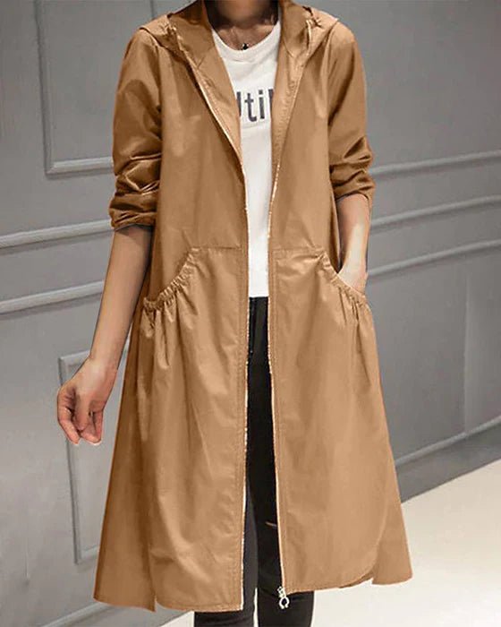 Giacca a vento lunga marrone da donna con cappuccio, tasche frontali e zip, indossata sopra una maglietta bianca. Moda casual autunnale.