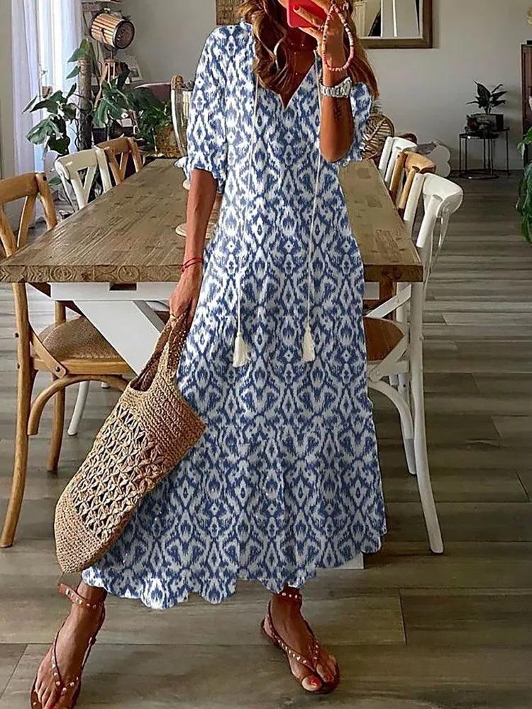 Donna con abito lungo boho blu e bianco, motivo etnico, borsa intrecciata, sandali, in sala da pranzo moderna. Moda estiva casual chic.