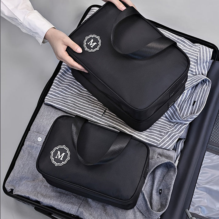 Utente che organizza valigia con borse da viaggio nere, logo "M", su camicie a righe. Accessori viaggio, organizzazione bagagli, valigia ordinata.