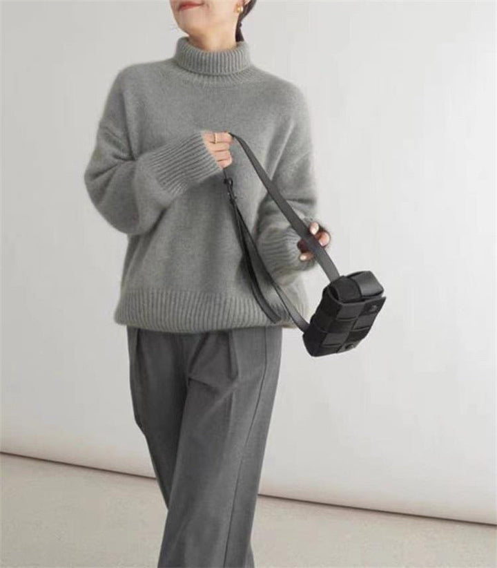 Donna con maglione grigio a collo alto, pantaloni grigi e borsa a tracolla nera. Moda autunnale, abbigliamento casual elegante.