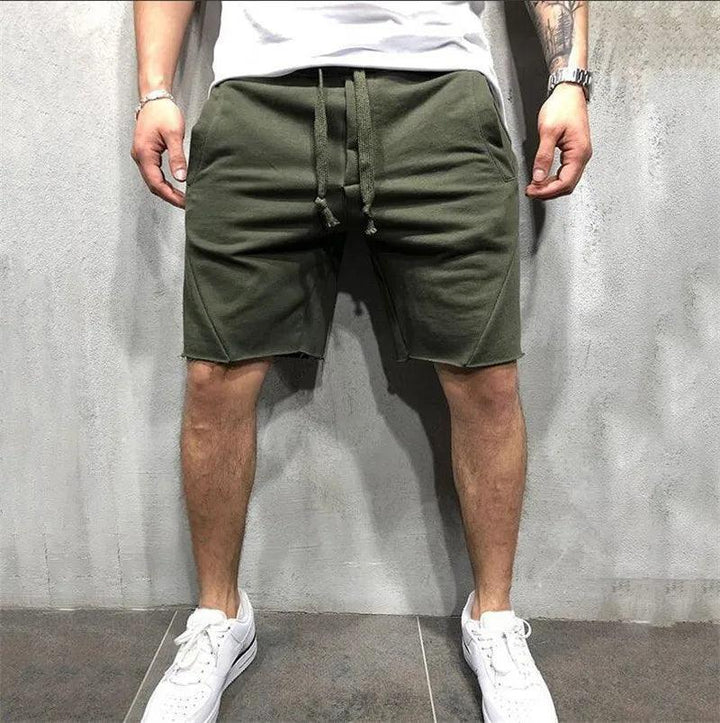 Uomo in pantaloncini verdi casual, scarpe da ginnastica bianche, sfondo grigio. Moda estiva maschile, abbigliamento sportivo, stile urbano.