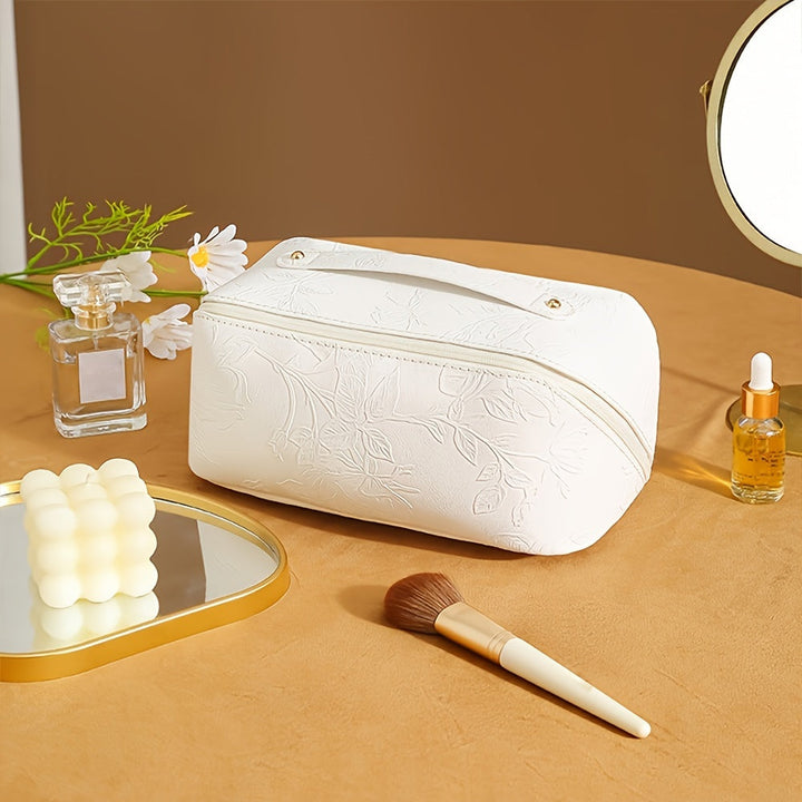 Borsa cosmetica bianca in pelle con motivo floreale, su tavolo con specchio, profumo, olio essenziale e pennello trucco. Accessori bellezza eleganti.