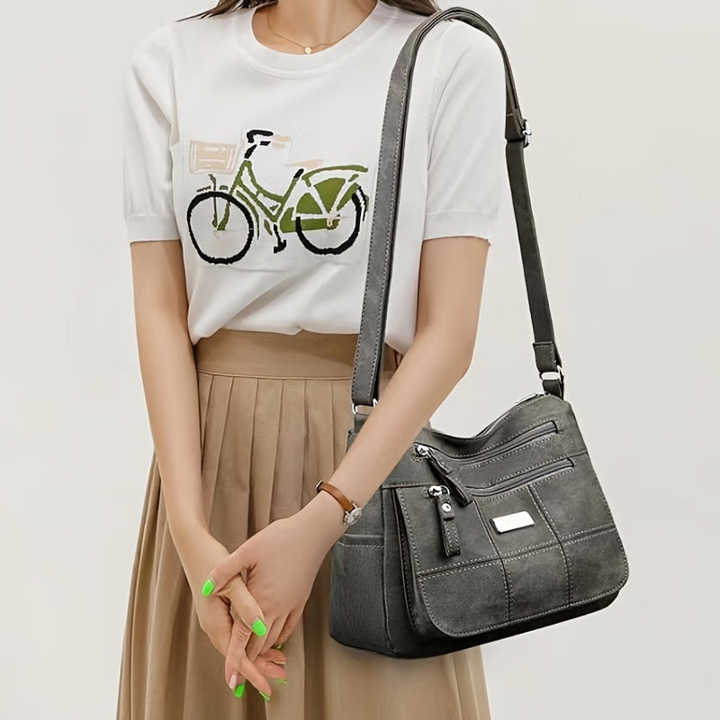 Borsa a tracolla in pelle grigia, design elegante con tasche multiple, indossata da donna con maglietta bianca e gonna beige. Accessorio moda femminile.