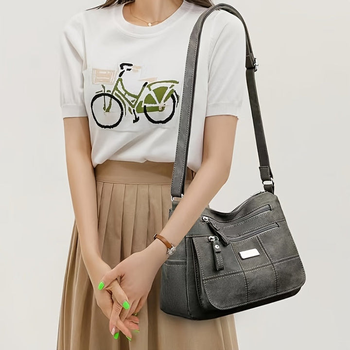Borsa a tracolla in pelle grigia, design elegante con tasche multiple, indossata da donna con maglietta bianca e gonna beige. Accessorio moda femminile.