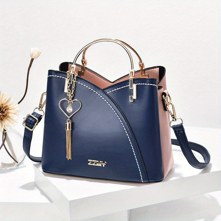 Borsa a mano elegante in pelle blu e rosa con manico dorato, tracolla regolabile e ciondolo a cuore. Accessorio moda donna di tendenza.