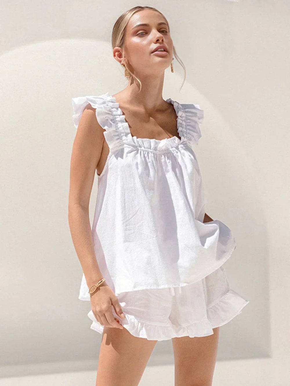 Ensemble femme en blanc, haut sans manches à volants avec short assorti, en tissu léger et respirant pour un confort estival.