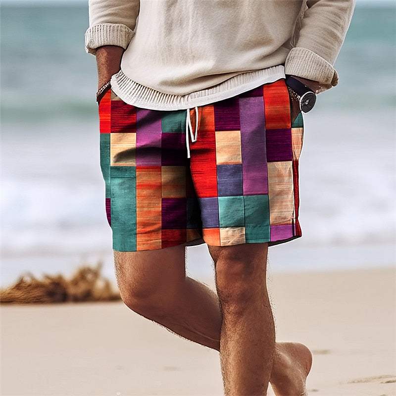 Uomo in spiaggia con pantaloncini patchwork colorati, maglione beige, orologio nero. Moda estiva, abbigliamento casual, stile vivace.