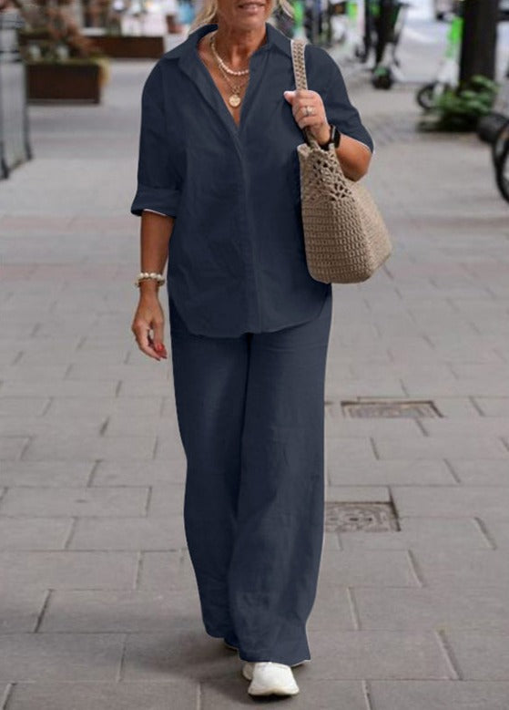 Donna con camicia blu scuro e pantaloni abbinati, borsa a tracolla beige, cammina su marciapiede cittadino. Moda casual elegante, abbigliamento donna.