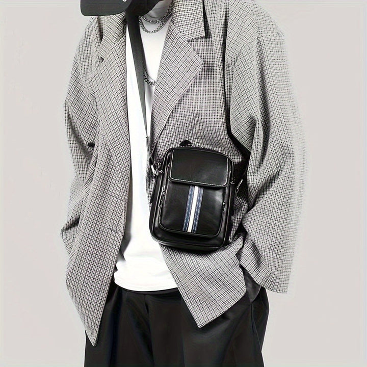 Giacca a quadri grigia da uomo con borsa a tracolla nera in pelle, dettagli a righe, abbinata a t-shirt bianca e pantaloni neri. Moda casual elegante.