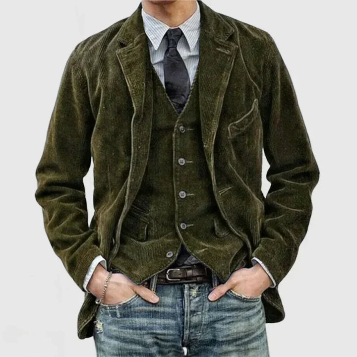 Giacca uomo in velluto a coste verde, abbinata a gilet e cravatta nera, camicia a righe e jeans. Look elegante e casual per moda maschile.