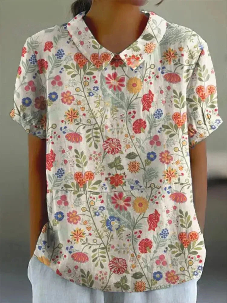 Camicia donna a maniche corte con stampa floreale colorata, colletto classico, sfondo bianco. Moda estiva casual, tessuto leggero e traspirante.