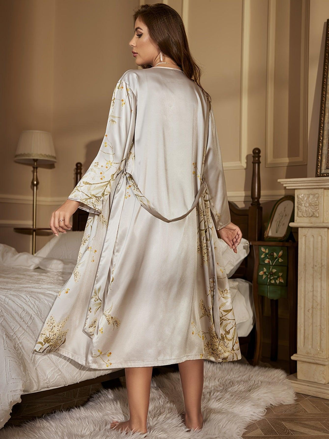 Donna in camera da letto indossa vestaglia di seta grigia con motivi floreali dorati, elegante e lussuosa, perfetta per comfort e stile notturno.