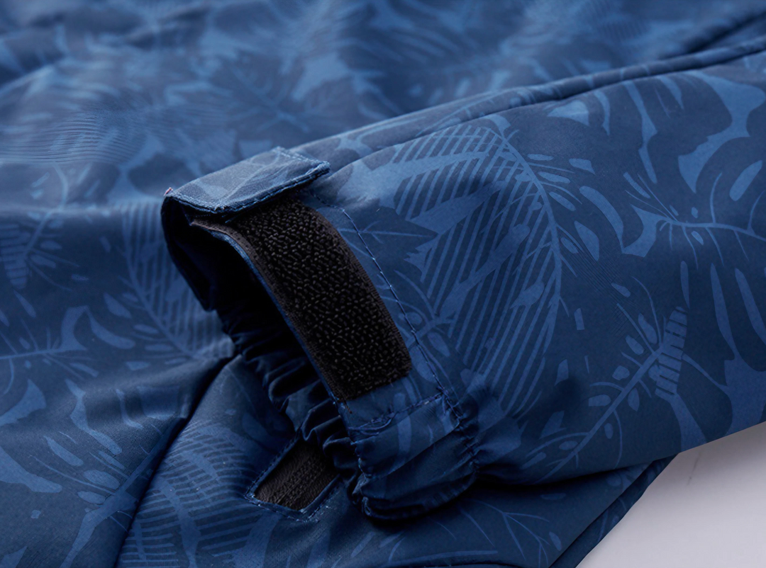 Giacca impermeabile blu con motivo foglie tropicali, chiusura in velcro. Abbigliamento outdoor, tessuto resistente, ideale per escursioni.