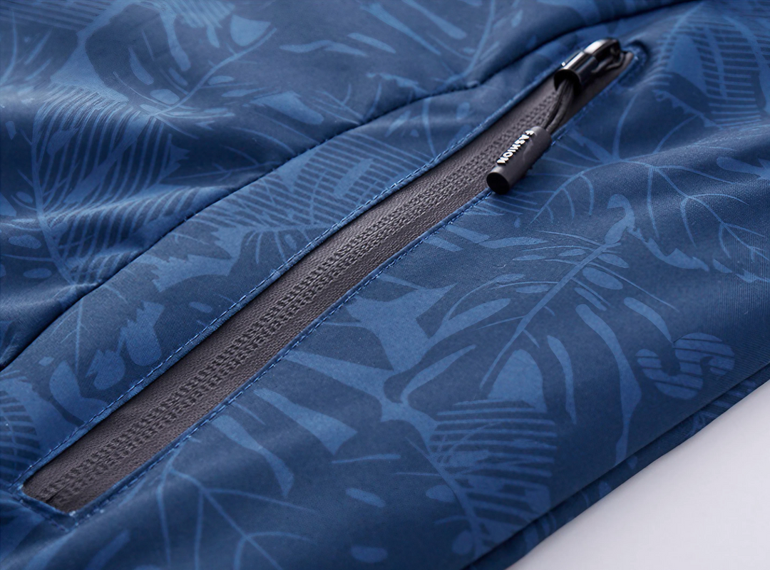 Giacca sportiva blu con motivo foglie tropicali, cerniera nera resistente, tessuto impermeabile. Ideale per attività outdoor e tempo libero.