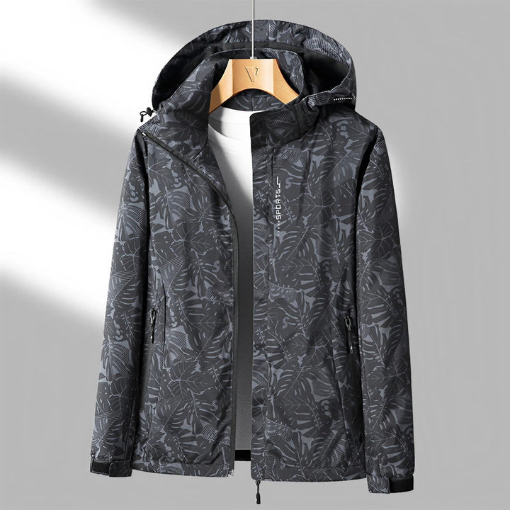 Giacca a vento impermeabile nera con motivo foglie, cappuccio regolabile, zip frontale, ideale per attività outdoor. Disponibile su appendiabiti.