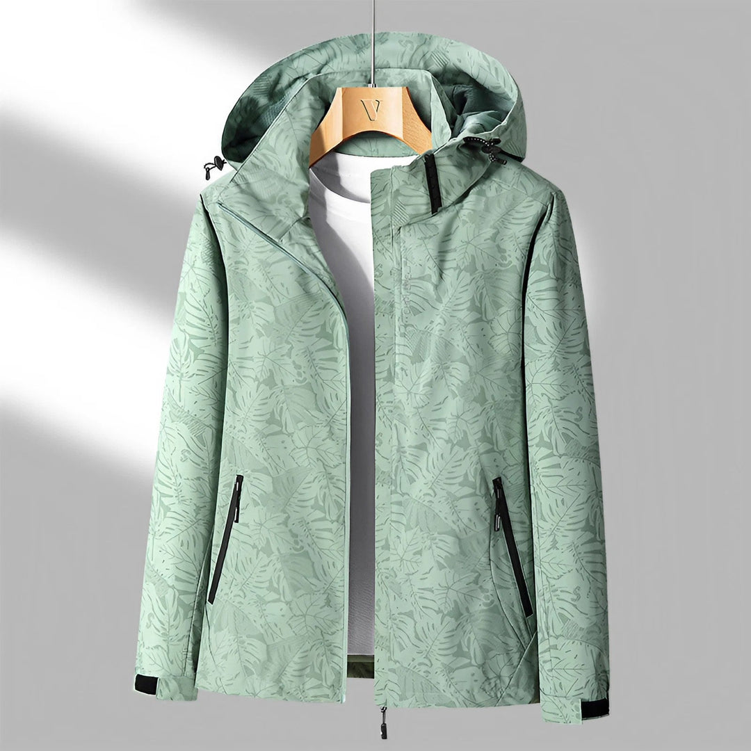 Giacca a vento verde con cappuccio, motivo foglie, zip nere, ideale per outdoor e sport. Design moderno, tessuto impermeabile, taglia media.
