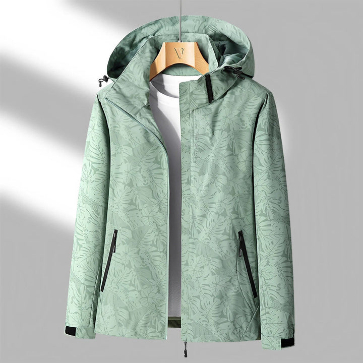 Giacca a vento verde con cappuccio, motivo foglie, zip nere, ideale per outdoor e sport. Design moderno, tessuto impermeabile, taglia media.