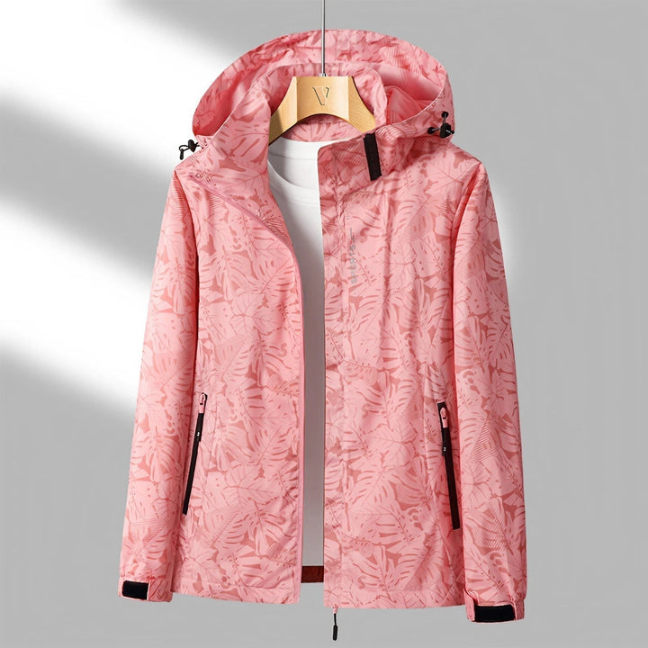 Giacca a vento rosa con cappuccio, motivo foglie, chiusura zip, tasche laterali, ideale per outdoor e sport. Design moderno e funzionale.