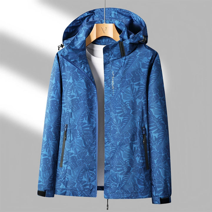 Giacca impermeabile blu con cappuccio, motivo foglie, chiusura zip, tasche laterali, ideale per outdoor e sport. Abbigliamento uomo resistente.