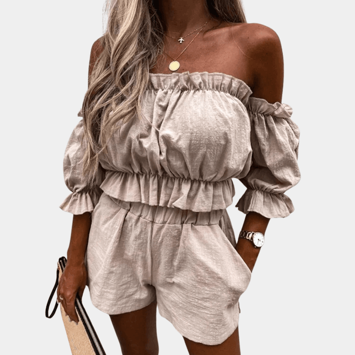 Donna con completo estivo beige, top a spalle scoperte e pantaloncini, accessoriata con borsa e orologio. Moda femminile casual elegante.