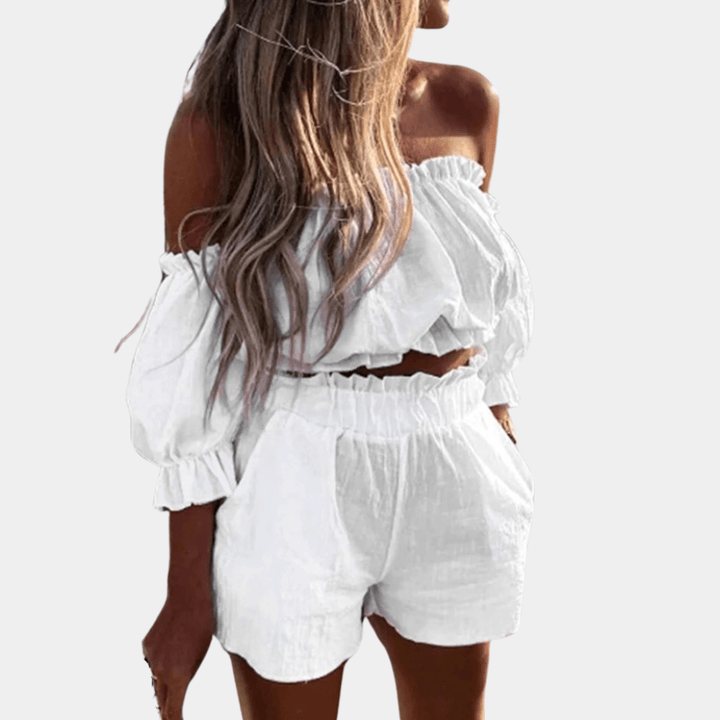 Donna con top e shorts bianchi, spalle scoperte, tessuto leggero. Moda estiva, abbigliamento casual elegante, look fresco e trendy.