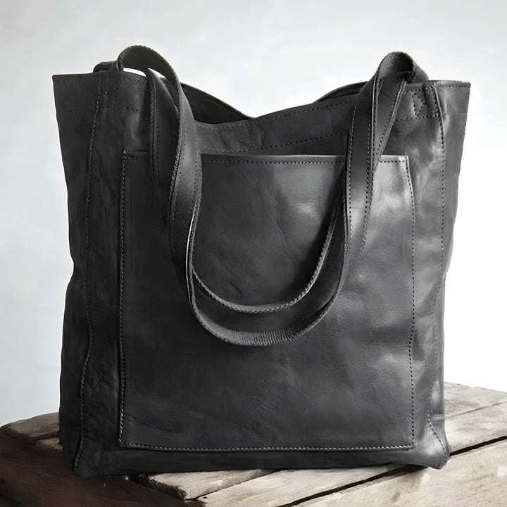 Borsa tote in pelle nera su tavolo di legno, design elegante e spazioso, ideale per moda donna, accessorio versatile e di tendenza.