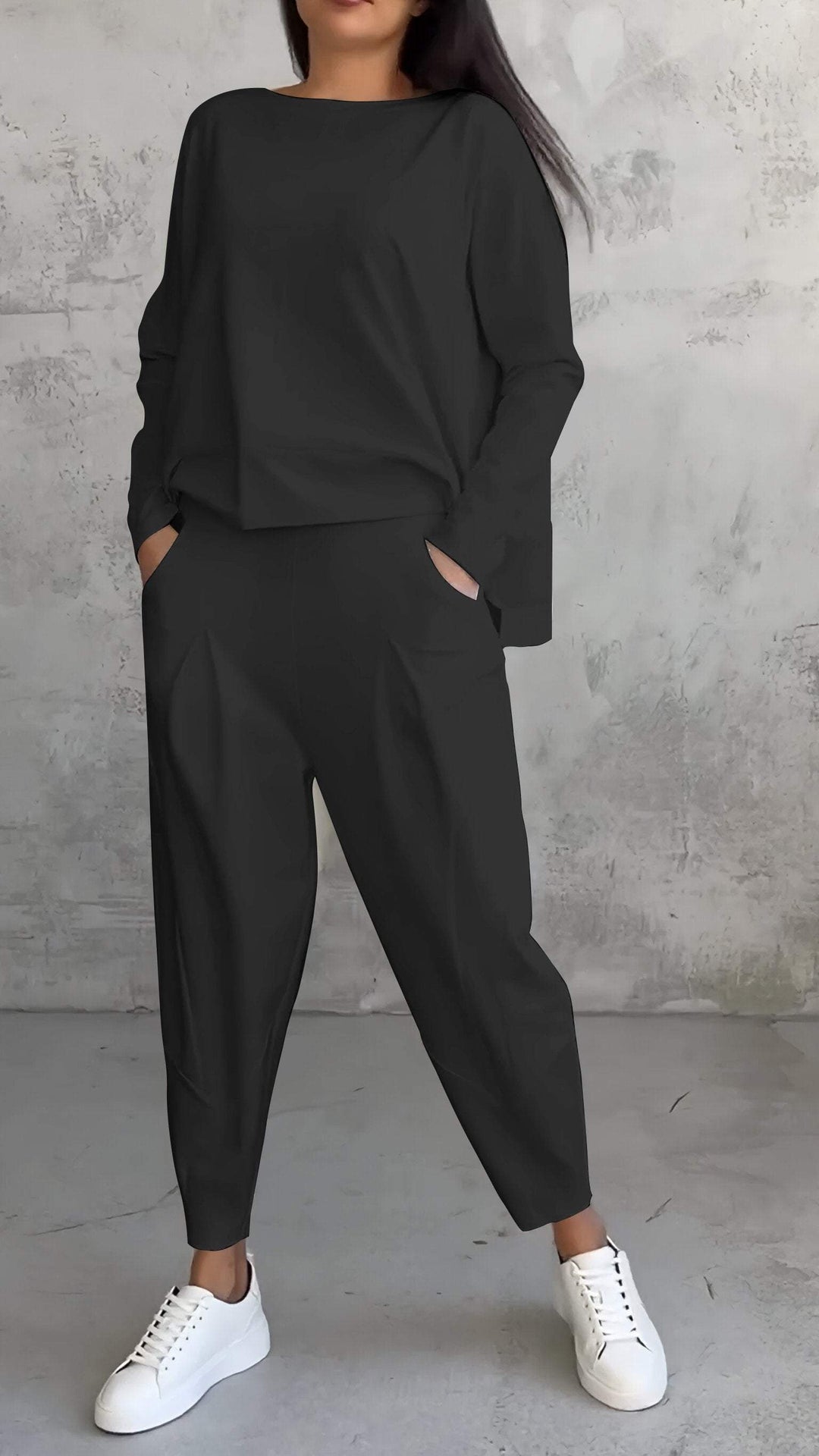 Donna in tuta nera casual con pantaloni larghi e maglia a maniche lunghe, indossa sneakers bianche. Look moderno e comodo per il tempo libero.