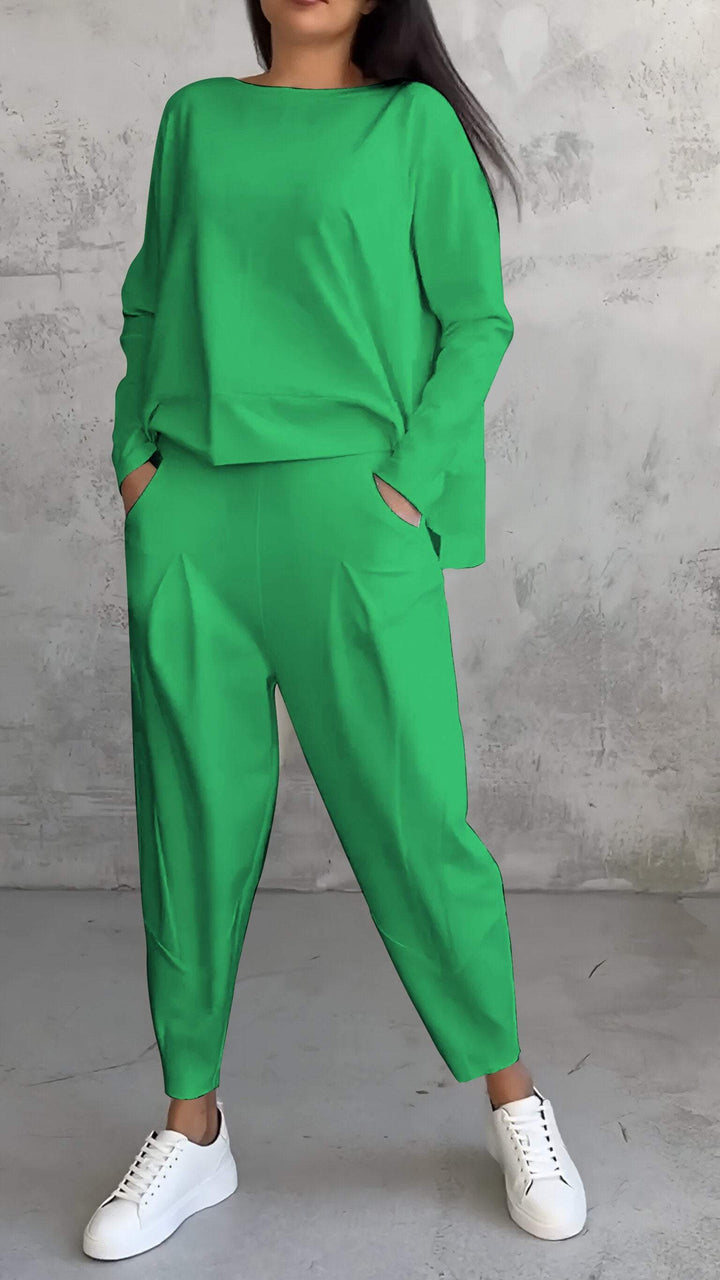 Donna in tuta verde brillante con pantaloni larghi e maglia a maniche lunghe, indossa sneakers bianche. Sfondo grigio minimalista.