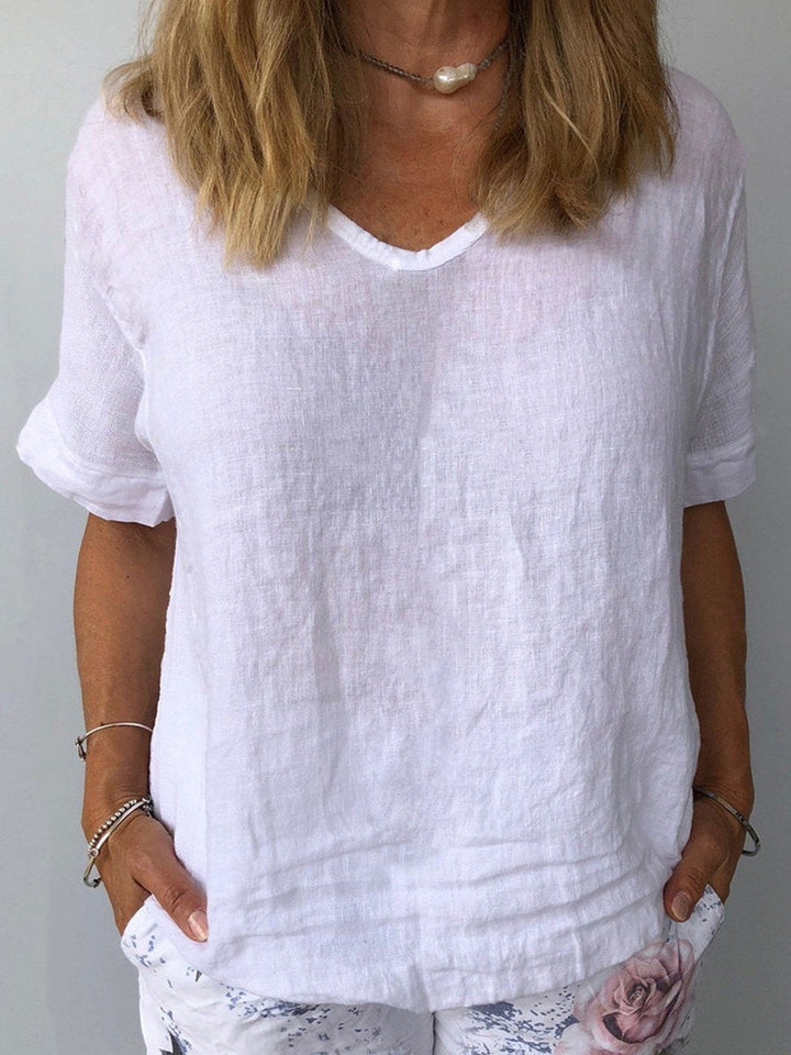 Donna con maglietta bianca in lino, scollo a V, maniche corte. Stile casual estivo, moda femminile, abbigliamento leggero e traspirante.