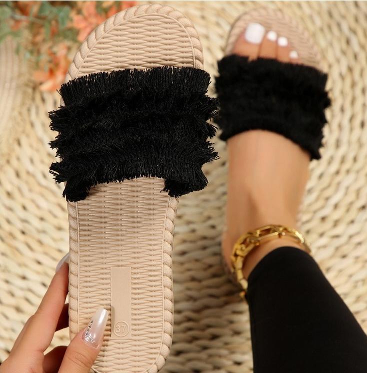Sandali estivi da donna con suola intrecciata beige e fascia nera in tessuto frangiato, indossati su tappeto chiaro. Accessorio moda casual.