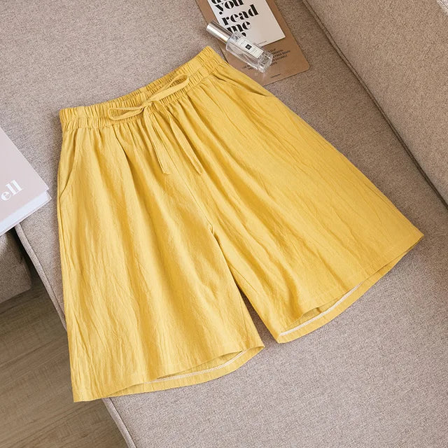 Pantaloncini gialli in lino su divano beige, con elastico in vita e tasche laterali. Moda estiva, abbigliamento casual, tessuto leggero.