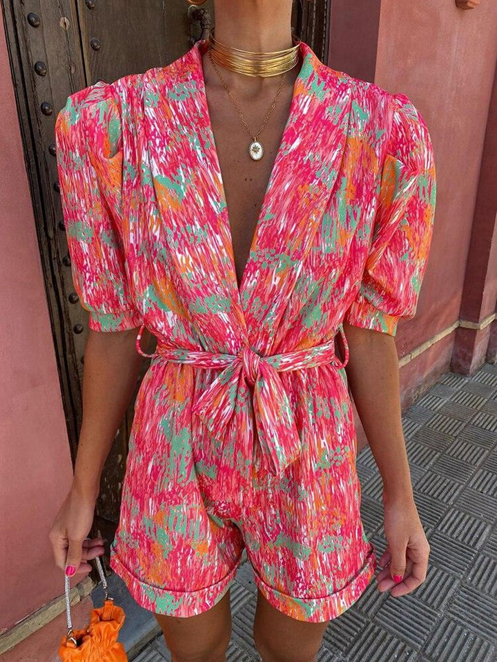 Tuta corta estiva donna, fantasia astratta rosa e arancione, maniche a sbuffo, cintura in vita, moda femminile, abbigliamento casual elegante.