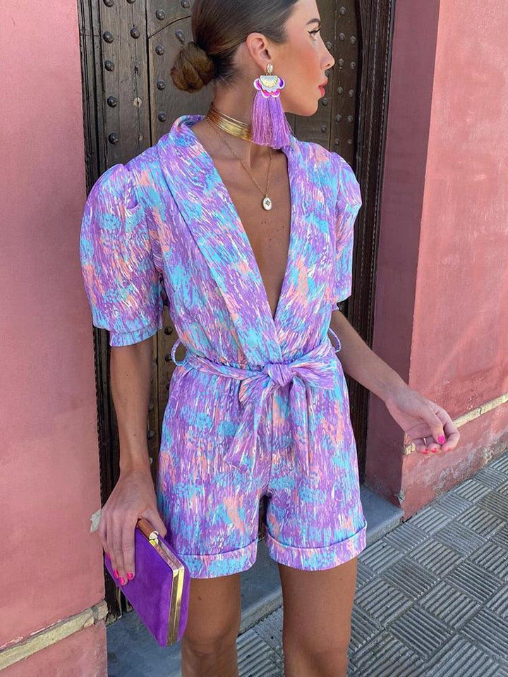 Donna con tuta estiva colorata, orecchini pendenti viola, collana dorata e pochette viola. Moda estiva, abbigliamento femminile elegante.