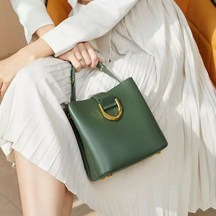 Donna con borsa a mano verde in pelle, design elegante, chiusura dorata, abito bianco plissettato. Accessorio moda femminile di lusso.