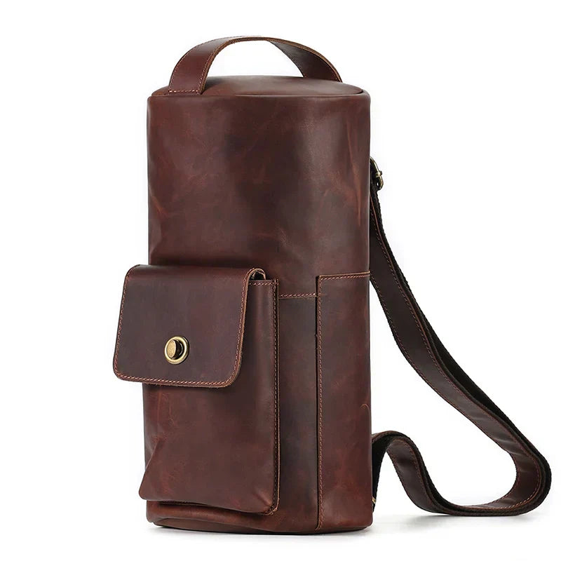 Borsa a tracolla in pelle marrone, design cilindrico, con tasca frontale e chiusura a bottone. Accessorio moda elegante e funzionale per uomo e donna.